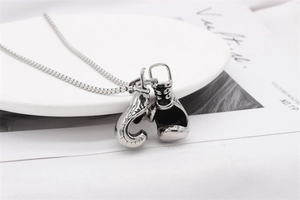 Detail of silver boxing glove pendants on a bead chain necklace over a ceramic plate