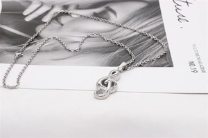Close-up of a silver treble clef pendant necklace on a minimalist magazine backdrop