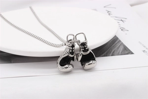 Macro detail of silver boxing glove pendants on a fine chain over a white tray