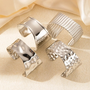 Macro shot of silver wide-band cuffs with smooth, striped, and hammered textures on silk