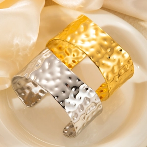Macro detail of gold and silver hammered metal wide open cuffs on elegant silk background