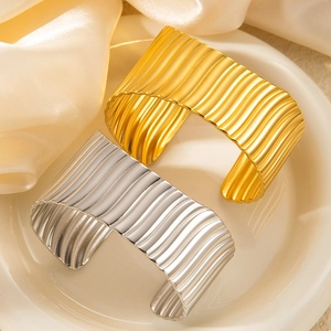 Detail showing two wavy textured cuff bracelets in gold and silver on a silk background