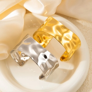 Detail of wide hammered metal bangles in gold and silver finish on white ceramic