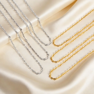 Detailed macro view of 2mm silver and gold cable chain necklaces on silk fabric