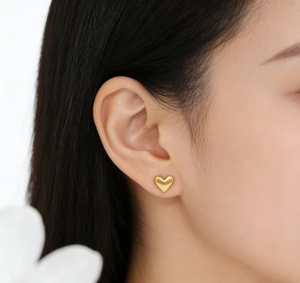 Close-up of minimalist gold heart stud earring worn on ear with polished finish