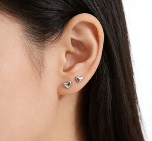 Macro shot of minimalist sterling silver heart stud earrings on model's ear lobe
