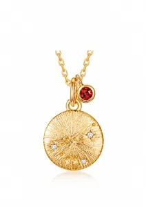 Detalle macro del colgante de constelación en oro cepillado con gema roja y circonitas
