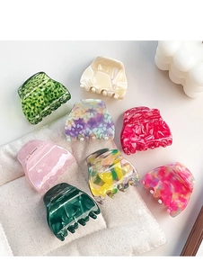 Flat lay of small colorful acetate hair claws in various patterns on a textured fabric
