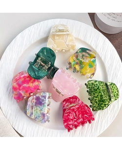 Flat lay of eight colorful acetate hair claws with marble patterns in a white ceramic dish