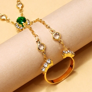 Detailed close-up of a gold slave bracelet featuring a green rhinestone and finger ring