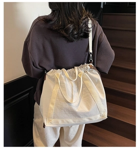 Detail van een crèmekleurige tote bag met trekkoord gedragen over de schouder