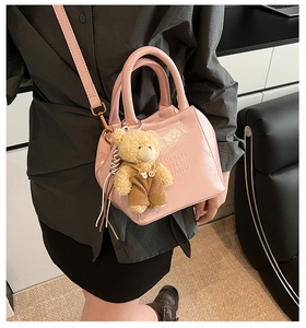 Detailed view of pink patent leather handbag featuring embossed logo and teddy bear charm