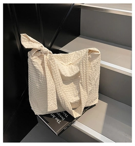 Detail of cream textured tote bag with a decorative knotted shoulder strap design