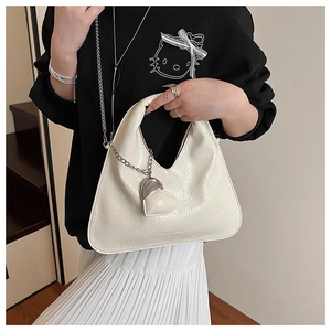 Detail of cream pleated crossbody bag with silver chain and heart charm held by model