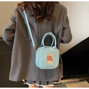 Close-up of a light blue glossy square handbag with a cartoon dog card holder detail