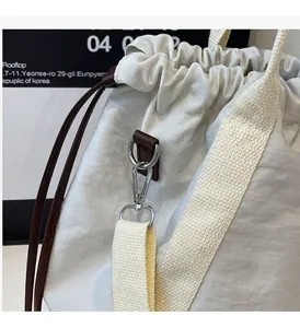 Detail van de zilveren metalen karabijnsluiting en bruin leren trekkoord op de witte tas