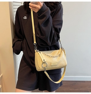 Detail of creamy yellow woven crossbody bag featuring metal chain and round charm