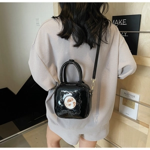 Detail of glossy black patent leather square crossbody bag with circular motif