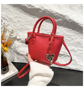 Gros plan du sac seau rouge montrant le cuir grainé et le pendentif cœur argenté