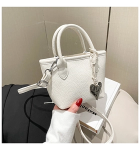 Detail of white litchi leather mini handbag featuring silver heart charm and crossbody strap