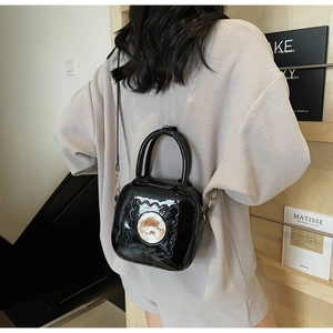 Model showing a black patent leather crossbody bag with a cartoon dog patch and wavy edges
