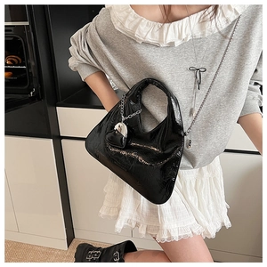 Detail of black patent leather crossbody bag with silver chain and heart charm accessory