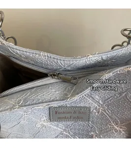 Close-up of light blue embroidered bag featuring a smooth silver zipper and leather tag