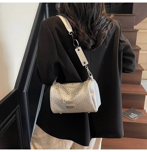Rear view of model with silver woven cylinder crossbody bag on indoor wooden stairs
