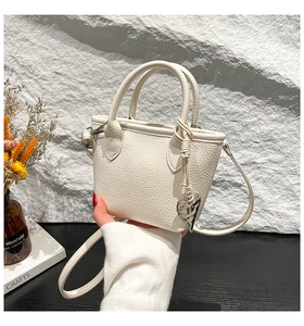 Détail du sac seau blanc à texture litchi avec un pendentif en métal en forme de cœur