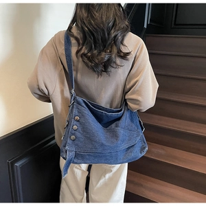 Back view of model wearing a large vintage denim crossbody tote with metal rivets