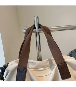 Detail view of reinforced brown leather strap patches and cross stitching on canvas tote bag