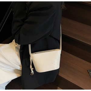 Détail du sac seau crème avec texture plissée brillante et pendentif métallique chic