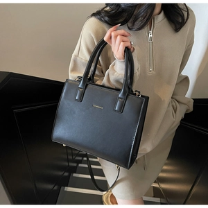 Detail of black vegan leather tote with gold logo and detachable shoulder strap on steps