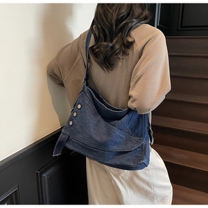 Detail of dark blue denim crossbody bag with metal buttons and adjustable strap on a model