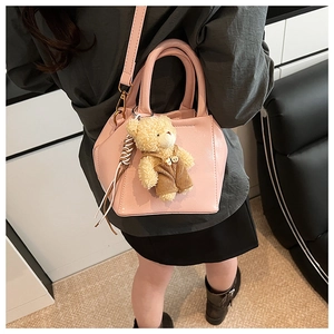 Rear view of pink leather shoulder bag with cute plush bear charm on a model