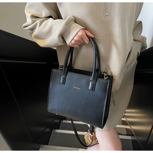 Detail of elegant black matte tote bag with gold lettering and slim shoulder strap