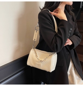 Detail of off-white woven texture shoulder bag with metal chain on black blazer