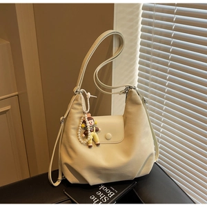 Close-up of a beige hobo shoulder bag featuring a pearl charm and stylish flap closure