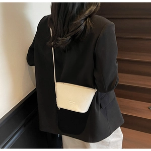 Détail d'un sac bandoulière en cuir texturé crème avec logo sur fond de blazer noir