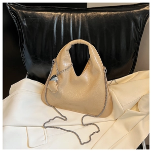 Detail view of apricot patent leather dumpling bag with silver chain and heart charm