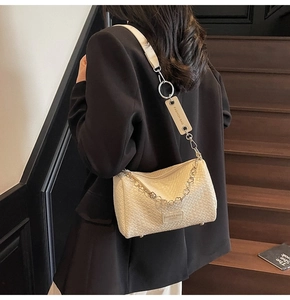 Detailed close-up of beige woven crossbody bag with silver floral chain and brand tag