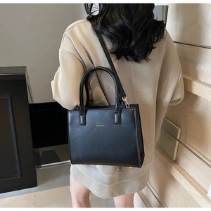 Detail view of a black leather tote bag featuring gold logo and detachable shoulder strap