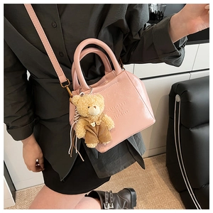 Detail of pink glossy leather tote bag featuring a teddy bear charm and embossed logo