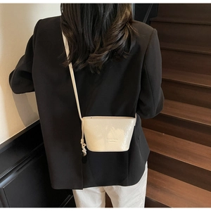 Détail du sac seau crème avec texture craquelée brillante et bandoulière à nœuds