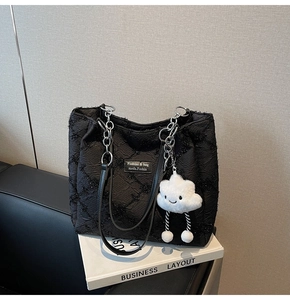 Detail of black tote bag with star patterns, silver chain strap, and white plush cloud charm
