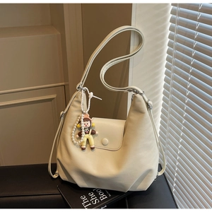 Detail of off-white canvas tote bag featuring pleated leather design and pearl doll charm