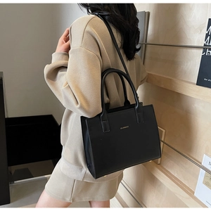 Detail of black matte leather tote bag with gold logo and adjustable shoulder strap