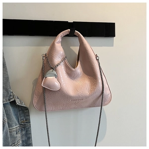 Detail of pink glossy pleated handbag with metal chain strap and heart charm