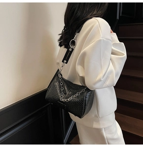 Close-up of black woven texture Boston bag with metal chain and wide branded strap