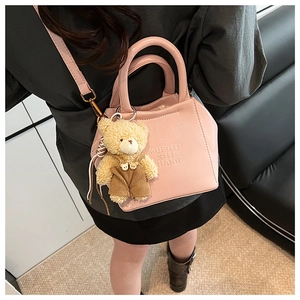 Pink crossbody bag detail featuring a teddy bear charm and embossed fashion text